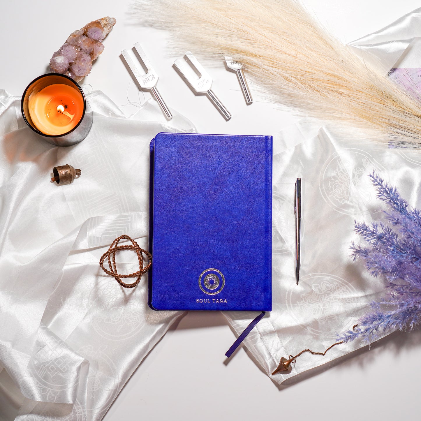Back cover of Cosmic starlight journal on a white cloth surrounded by a candle and few tuning forks and crystal