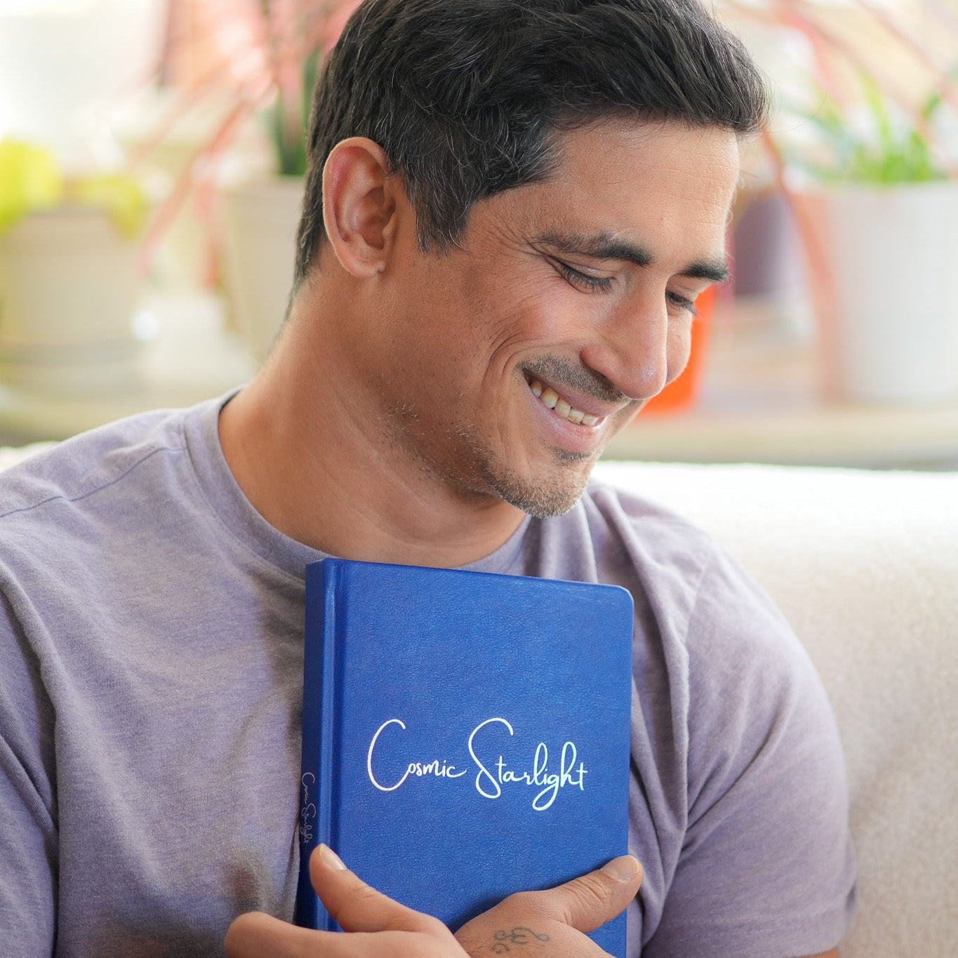 Man holding a blue book with 'Cosmic starlight' on it, surrounded by plants.