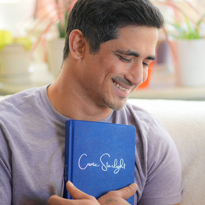 Man holding a blue book with 'Cosmic starlight' on it, surrounded by plants.